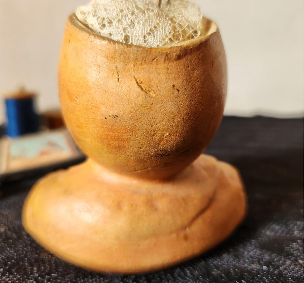A handmade ceramic vessel with a bulbous, rounded top and a wide, flared base, shown filled with a white lace fabric. The ceramic has a warm, earthy ochre-brown glaze.