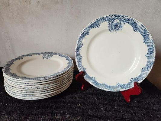 A collection of white ceramic plates with a blue floral border and a central design. One plate is displayed on a red stand. The plates have a vintage aesthetic, suitable for serving food.